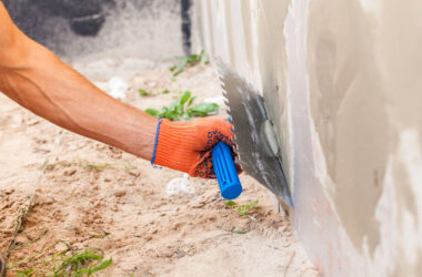 Construction worker plastering a wall and house foundation with trowel